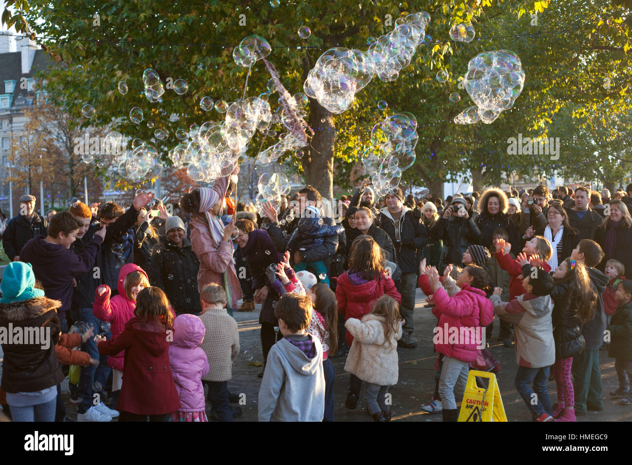 I bambini e i loro genitori si radunano un esecutore di strada lasciando una scia di gigantesche bolle sulla South Bank di Londra Foto Stock