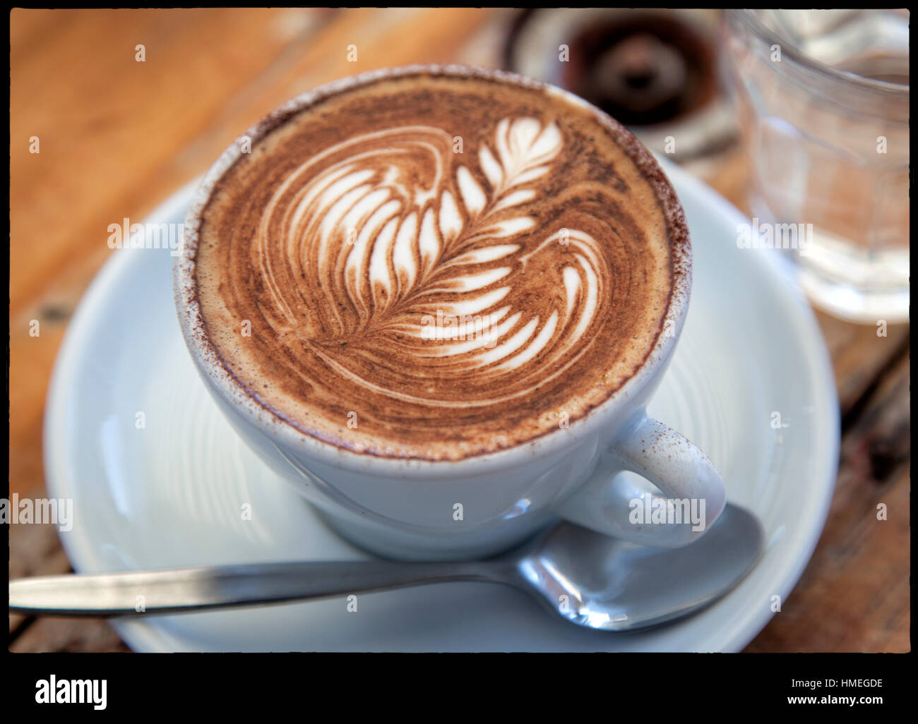 Un perfettamente realizzato un cappuccino con un bicchiere di acqua su un rustico outdoor cafe tabella Foto Stock