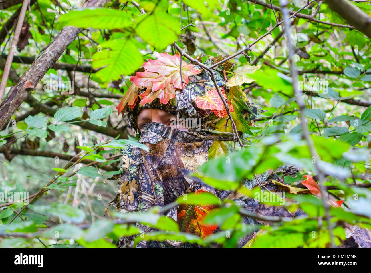 Hunter wildlife watcher in Abbigliamento camouflage nasconde nella boccola in una foresta. Foto Stock