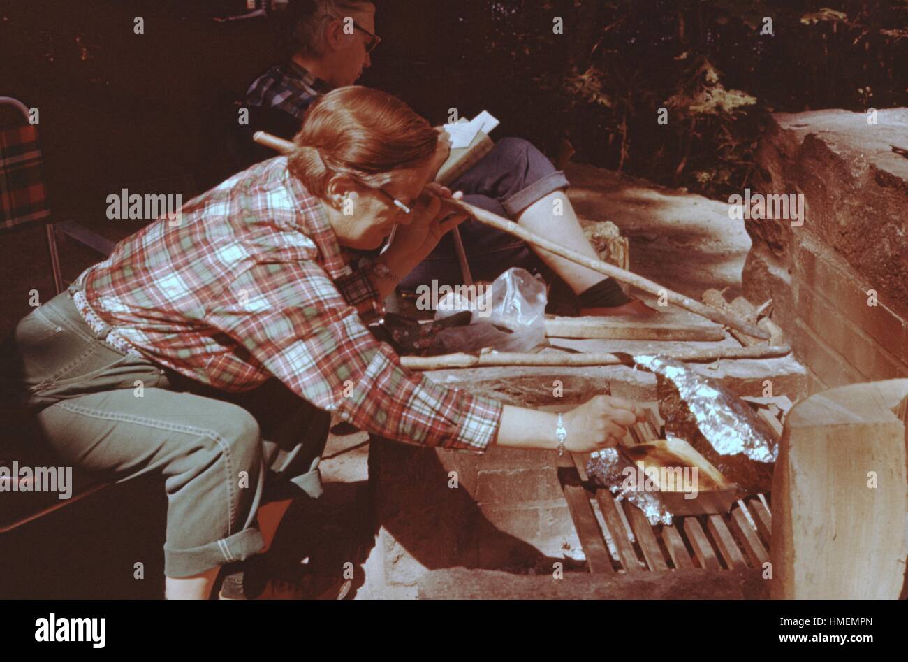 Persona che si allunga verso un piatto di cibo cucinato su una griglia a carbone durante una cottura, tenendo in mano un bastone, Maidstone foresta, Vermont, USA, 1955. Credito Foto Collezione Smith/Gado/Getty Images. Foto Stock