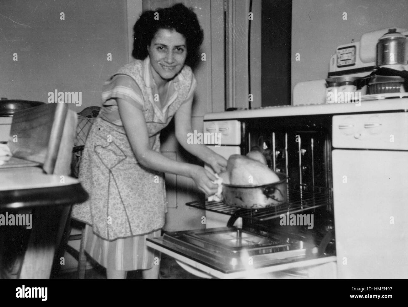 La Giornata del ringraziamento, una giovane donna in un grembiule in piedi nella sua cucina e di posizionamento di una Turchia su una teglia da forno in un forno, sorridente alla fotocamera, 1960. Credito Foto Collezione Smith/Gado/Getty Images. Foto Stock