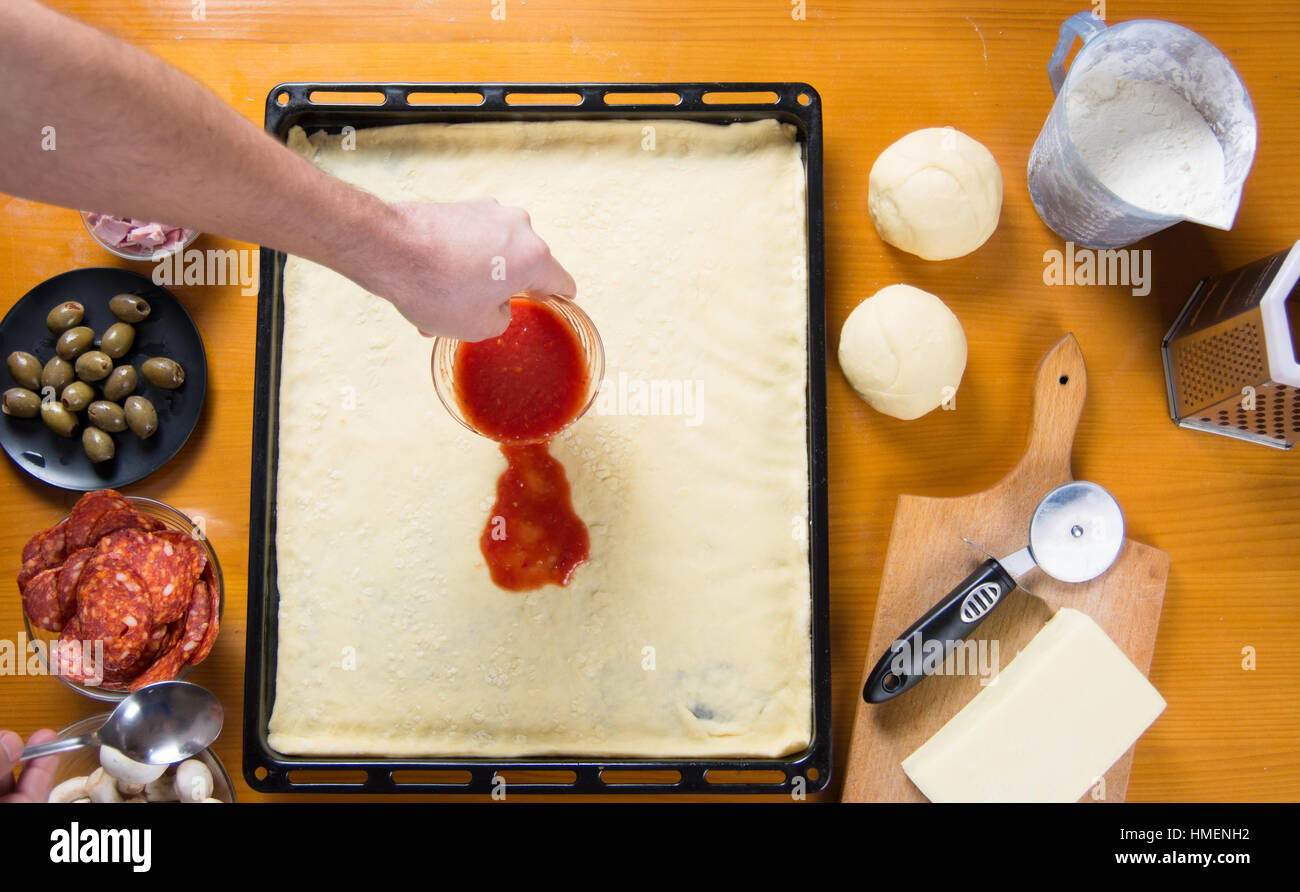 Uomo di mettere la salsa di pomodoro sulle materie di base per pizza Foto Stock