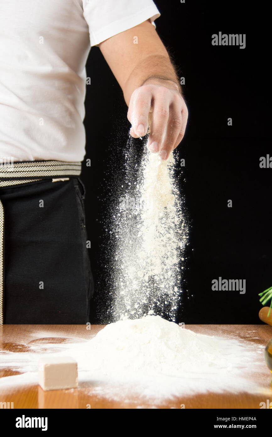 Voce maschile baker aggiungendo farina sulla pila a mano Foto Stock