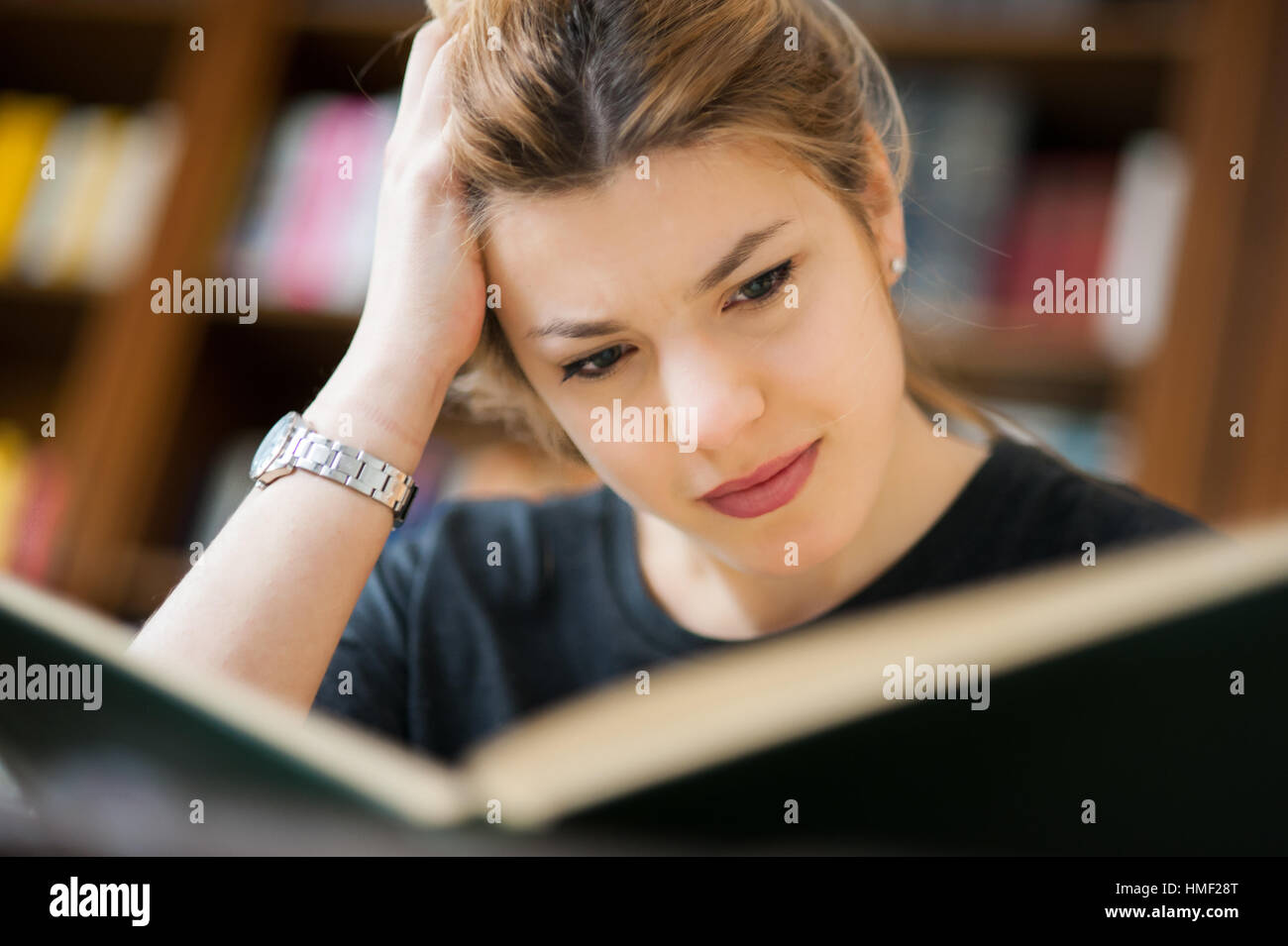 Giovane studentessa in biblioteca, ritratto mentre focalizzata studiando, fuori fuoco Libreria in background Foto Stock