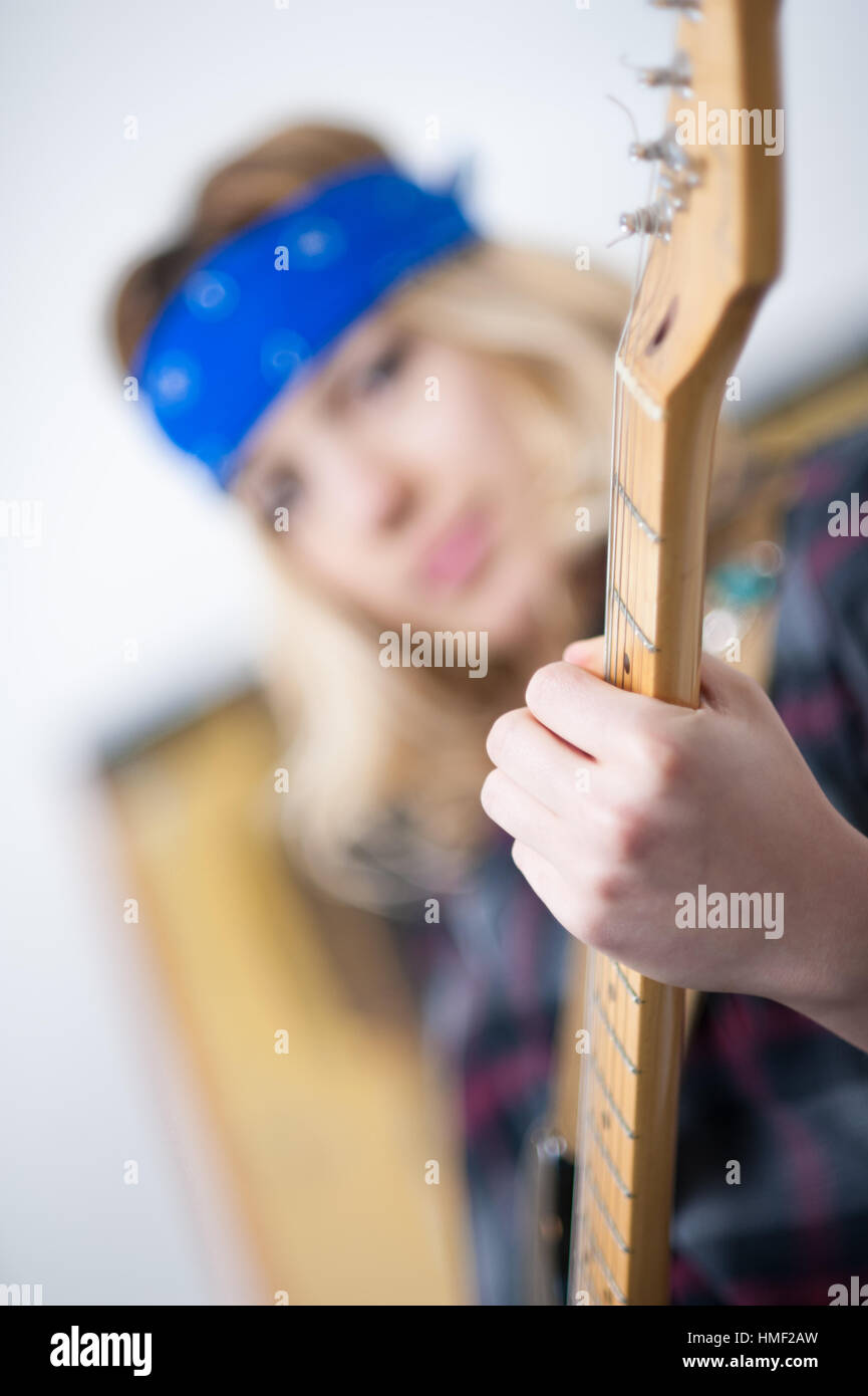 Donna suonare la chitarra elettrica, dettaglio mano sul collo di legno, volto umano al di fuori della messa a fuoco in background Foto Stock