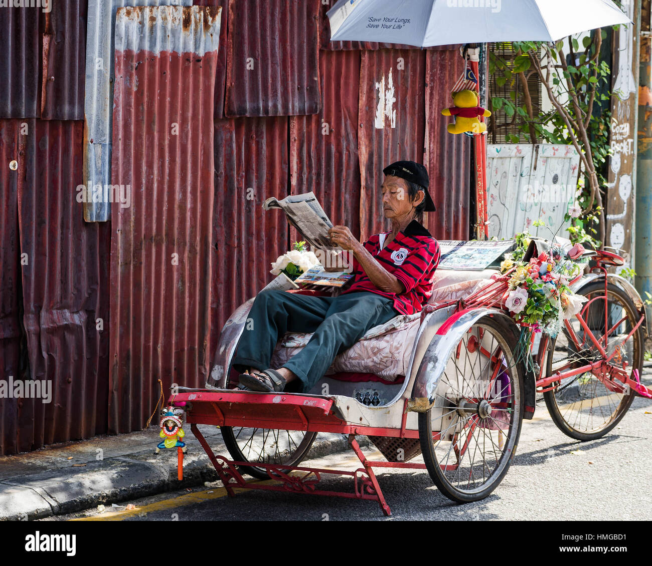 Un turista rickshaw driver fuoriuscite di sole di mezzogiorno per leggere il giornale nella storica Georgetown, in Penang (Malesia) Foto Stock