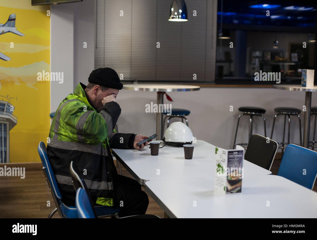 Stanco lavoratore avente un tè o un caffè break, guardando il suo cellulare o telefono cellulare Foto Stock