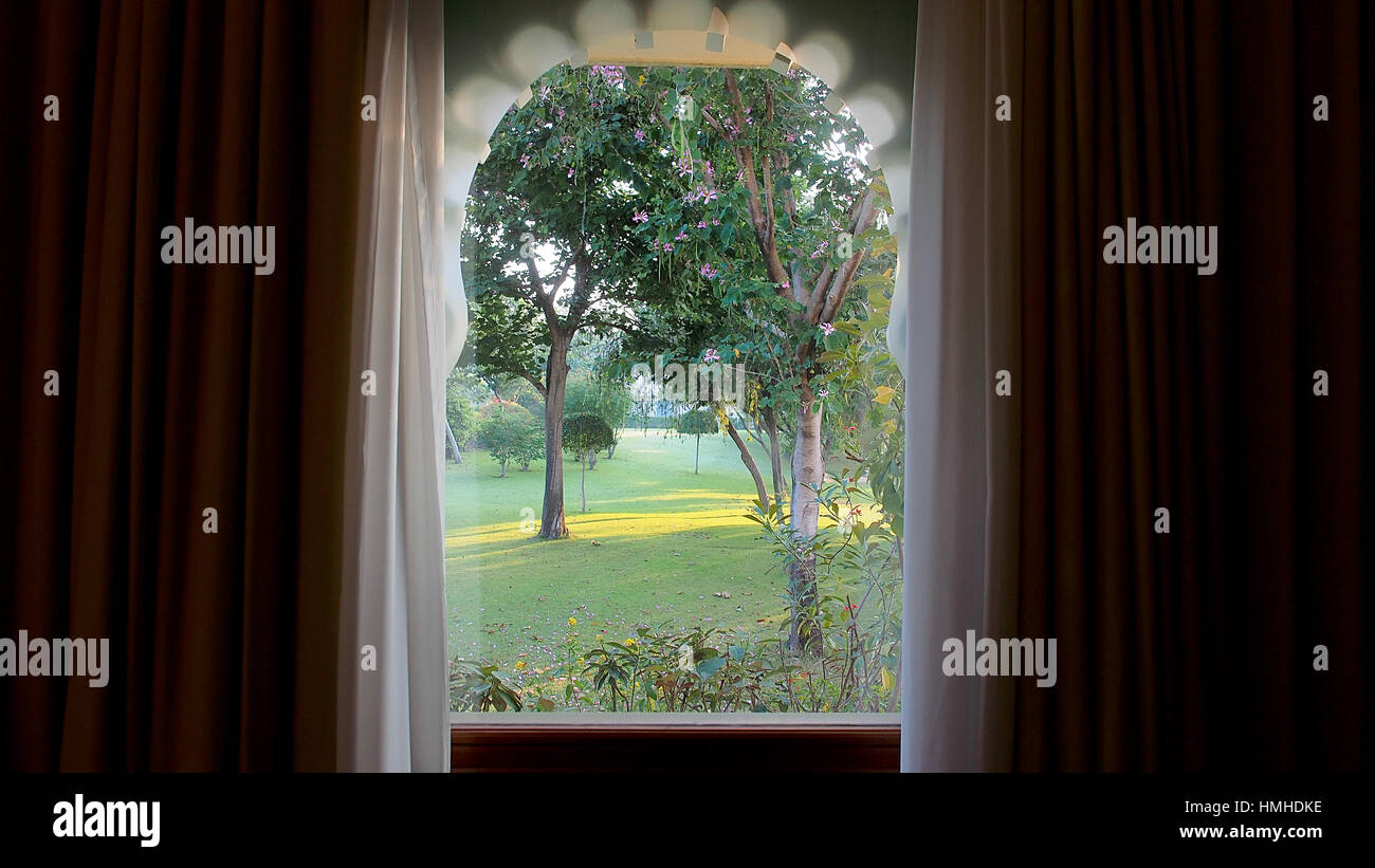 Vista sul giardino attraverso una forma curva finestra con tende su entrambi i lati, archi, vetro Foto Stock