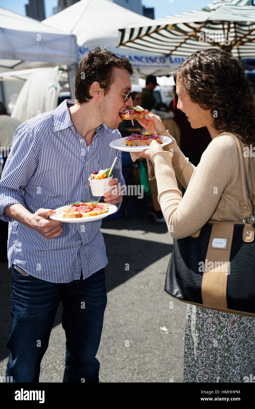 Coppia giovane Condividendo cibo ad un festival di strada di San Francisco, California Foto Stock