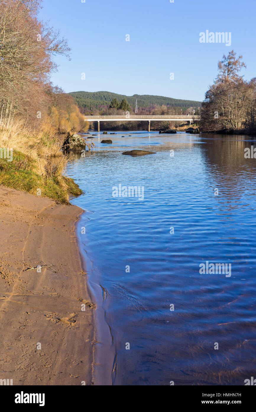 Spiaggia di sabbia sulle rive di un fiume con un ponte in background. Cielo azzurro e sole. Paesaggio invernale con alberi di nudo. Foto Stock