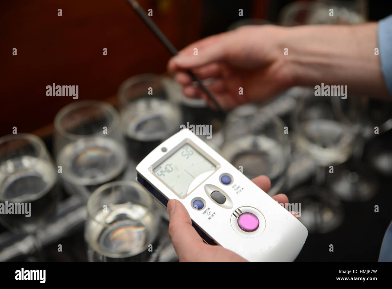 Un musicista tunes un set di bicchieri di vino parzialmente riempita con acqua per fare una gamma completa di note per un concerto di prestazioni Foto Stock