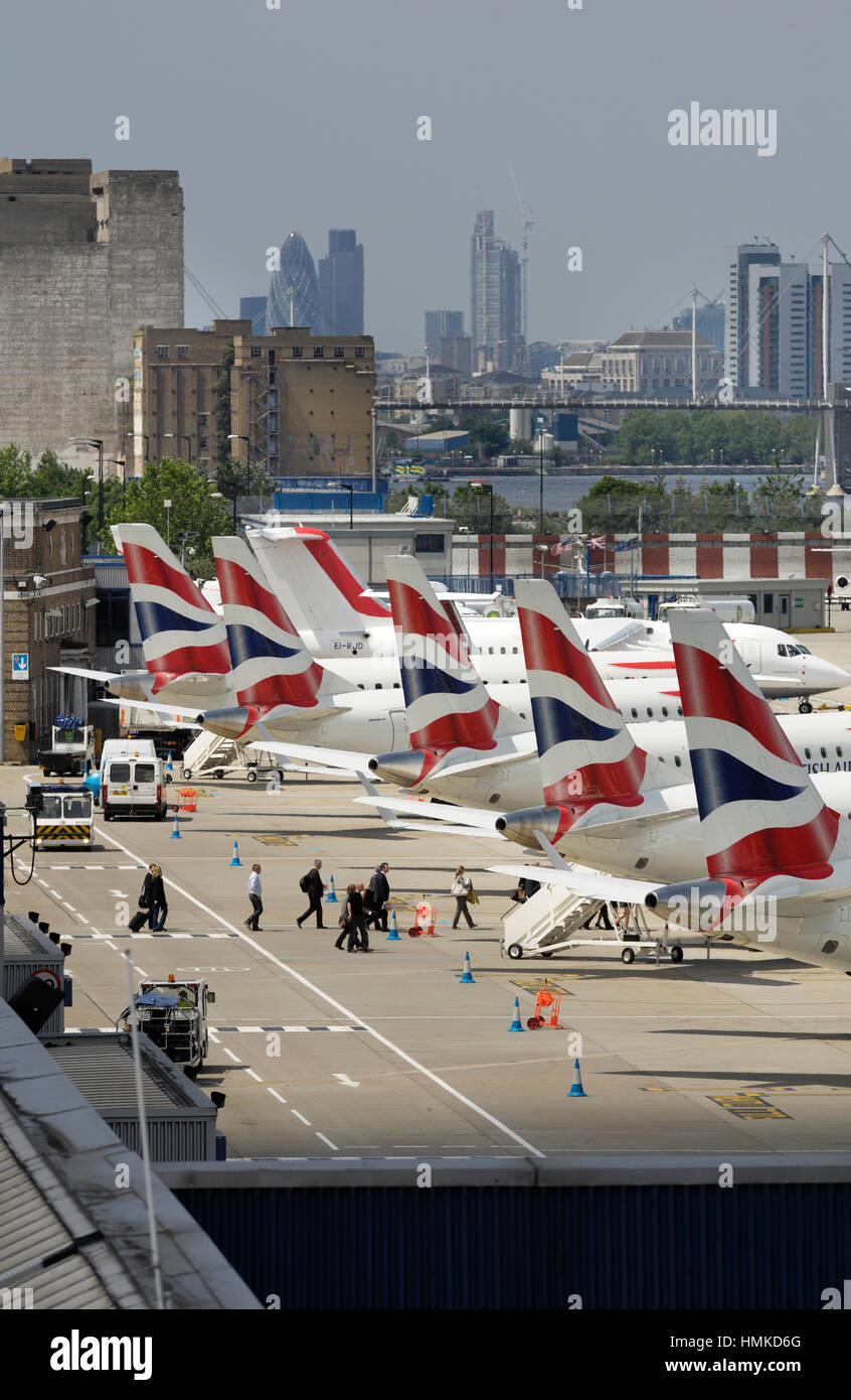 Tail-pinne di British Airways BA CityFlyer Embraer 170s parcheggiata in una riga a Londra città con grattacieli dietro Foto Stock