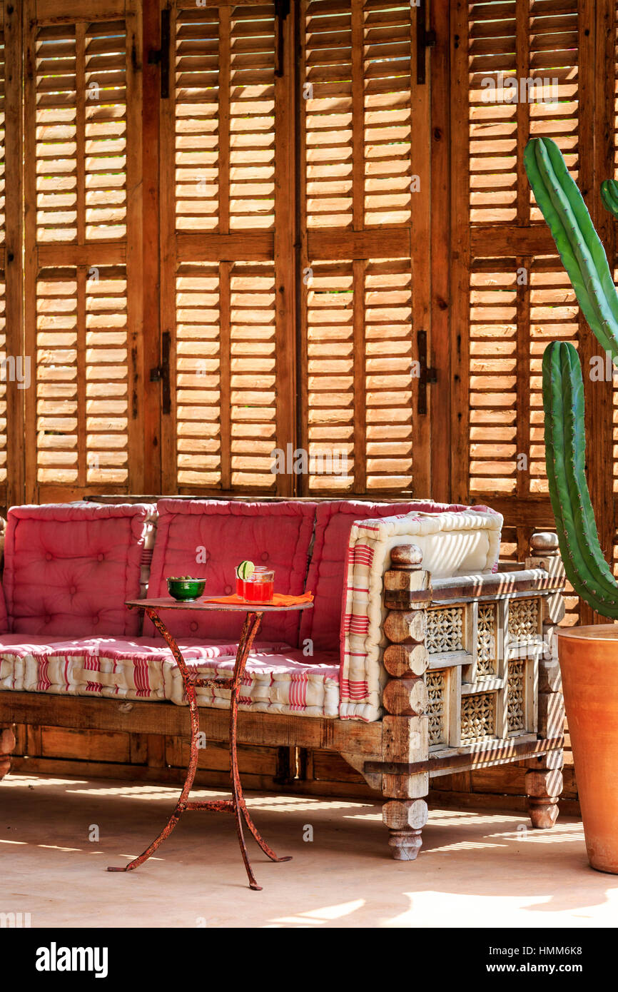Decorativi esterni panca in legno con cuscini e tavolo laterale con bevande, cactus e sfondo con copertura in estate francia Foto Stock