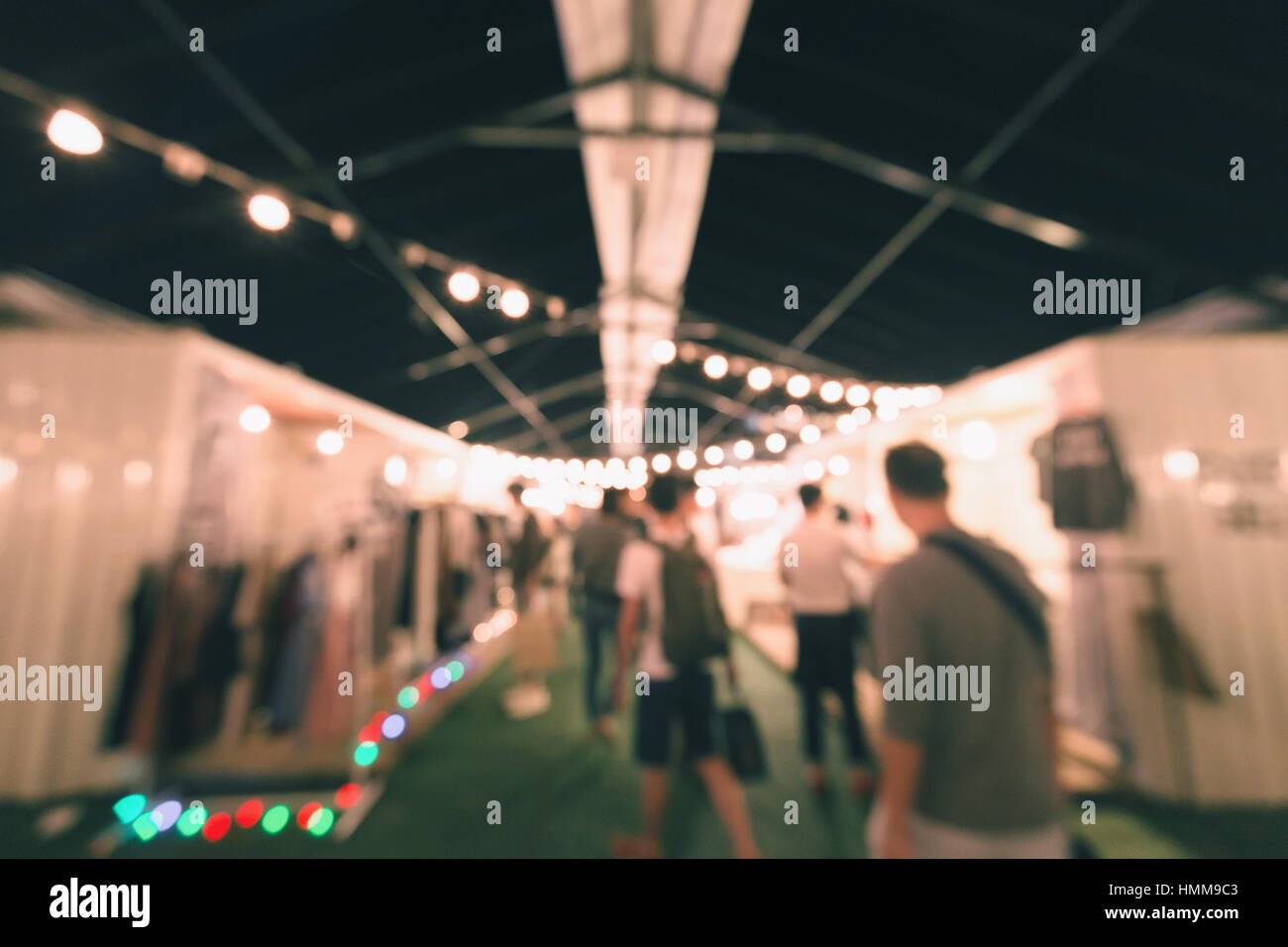Sfocata scena di esterno notte decorato di mercato dalle lampade appese sul soffitto. La gente camminare intorno per vedere i prodotti. Foto Stock
