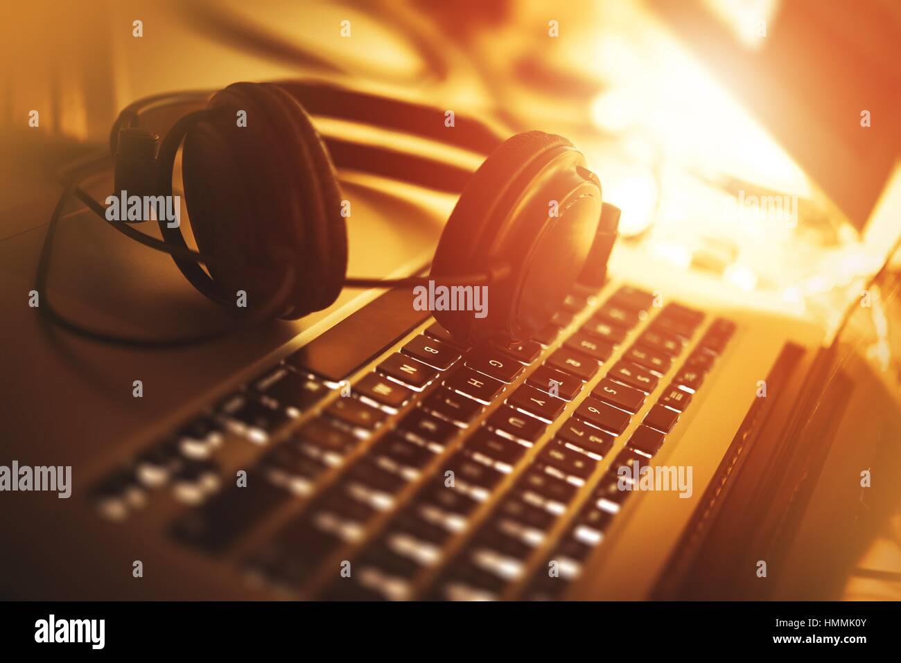 Ascoltare musica mentre lavora. Computer portatile e cuffie moderne Closeup Photo. Reddish colori caldi. Foto Stock