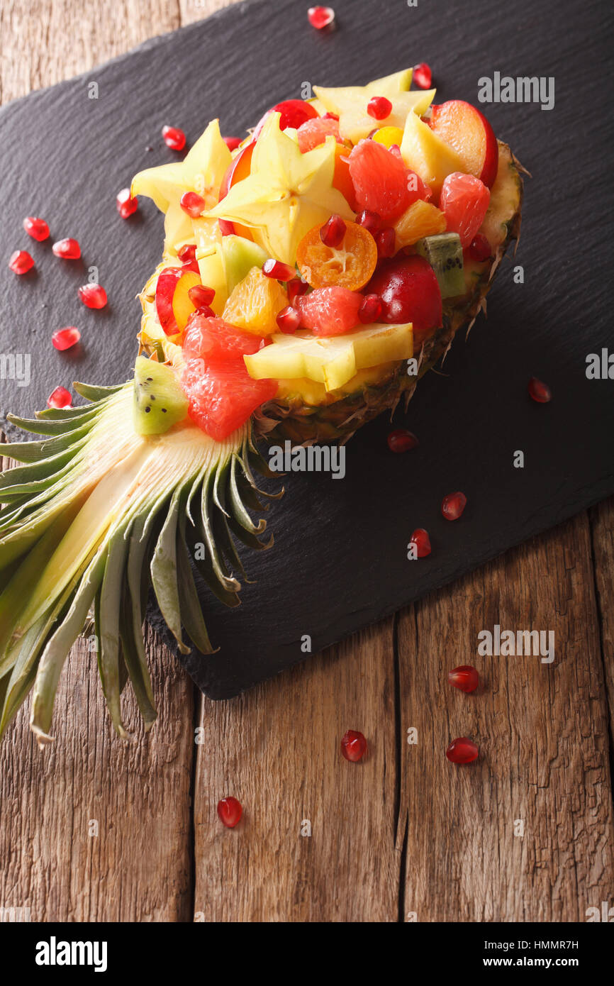 Ananas ripieni di frutta, kiwi kumquat, carambole, melograno, arancio, prugna closeup sul piano verticale. Foto Stock