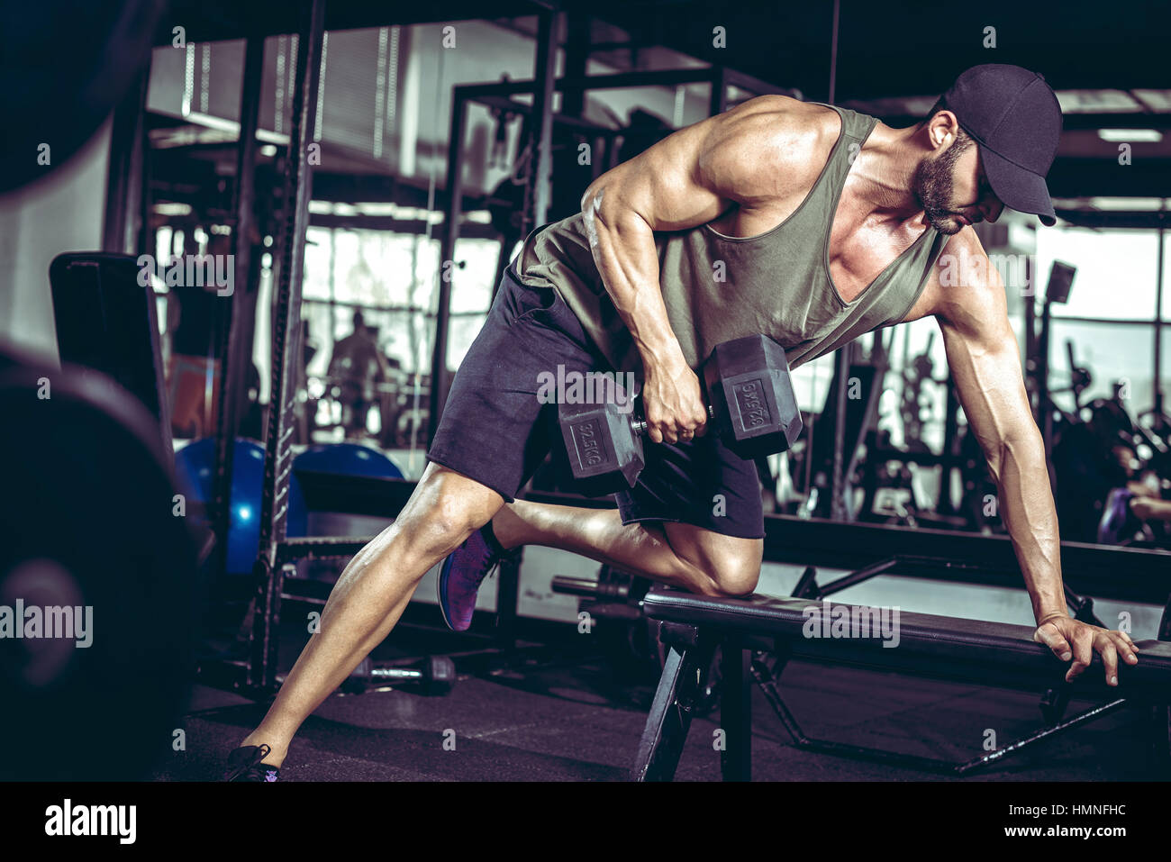 Bel giovane maschio adulto facendo uno-arm dumbbell righe sul banco in una palestra moderna Foto Stock
