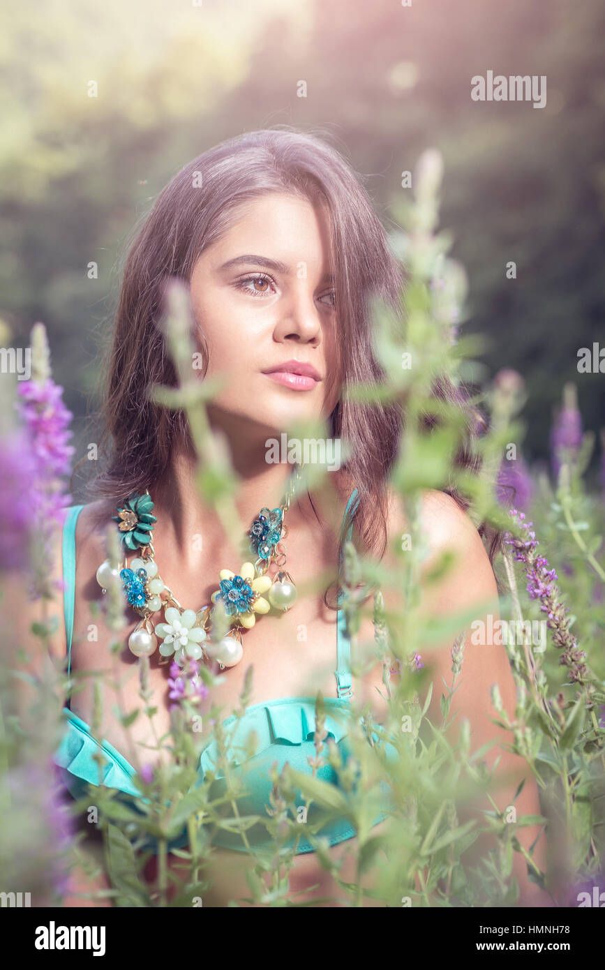 Giovane e bella ragazza in piedi in erba alta e fiori sulla banca del fiume di indossare reggiseno e jeans corti. Foto Stock