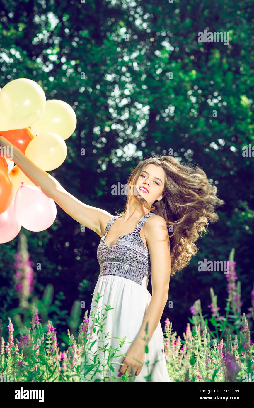 Ragazza in natura azienda palloncini indossando abito bianco Foto Stock