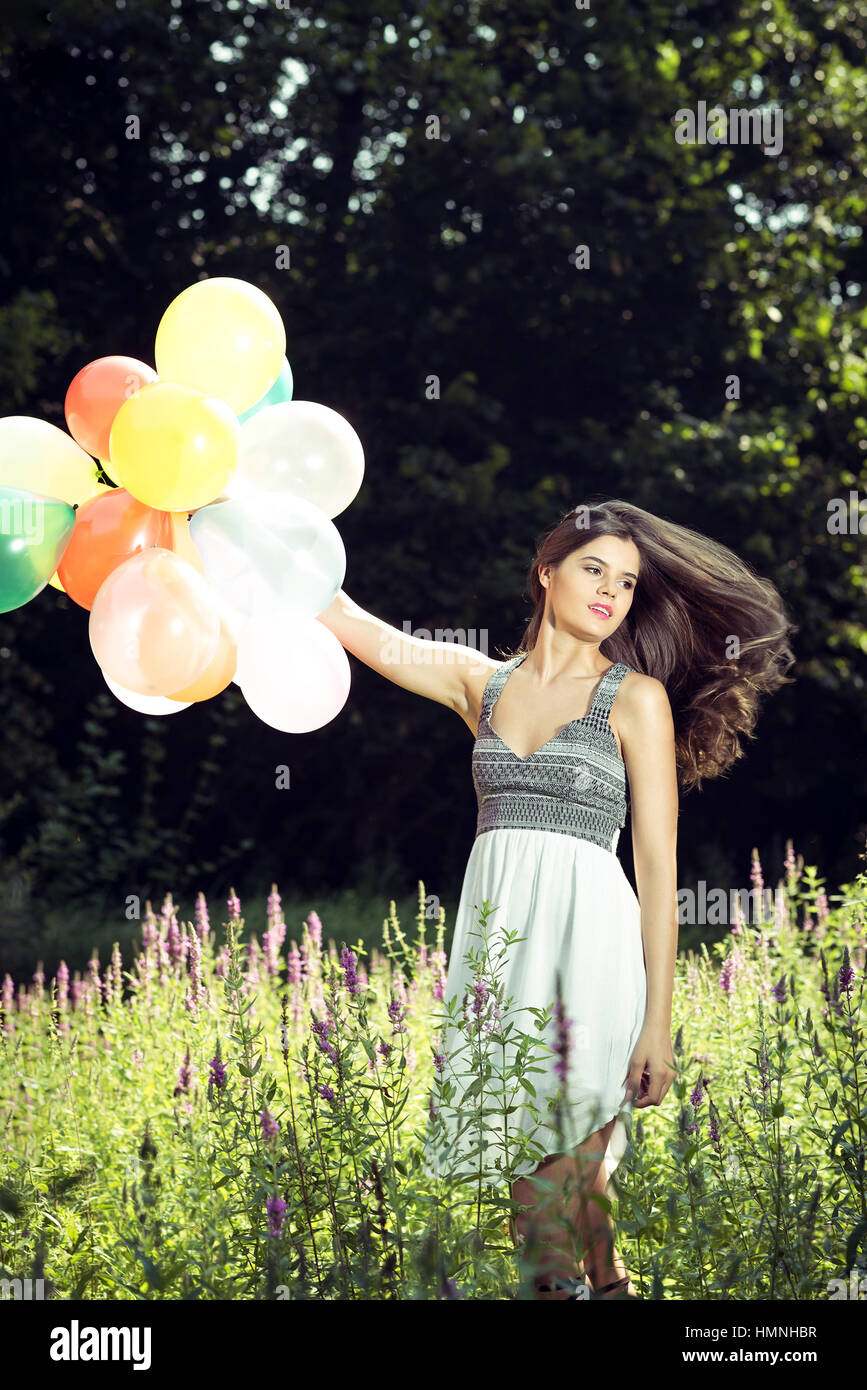 Ragazza in natura azienda palloncini indossando abito bianco Foto Stock