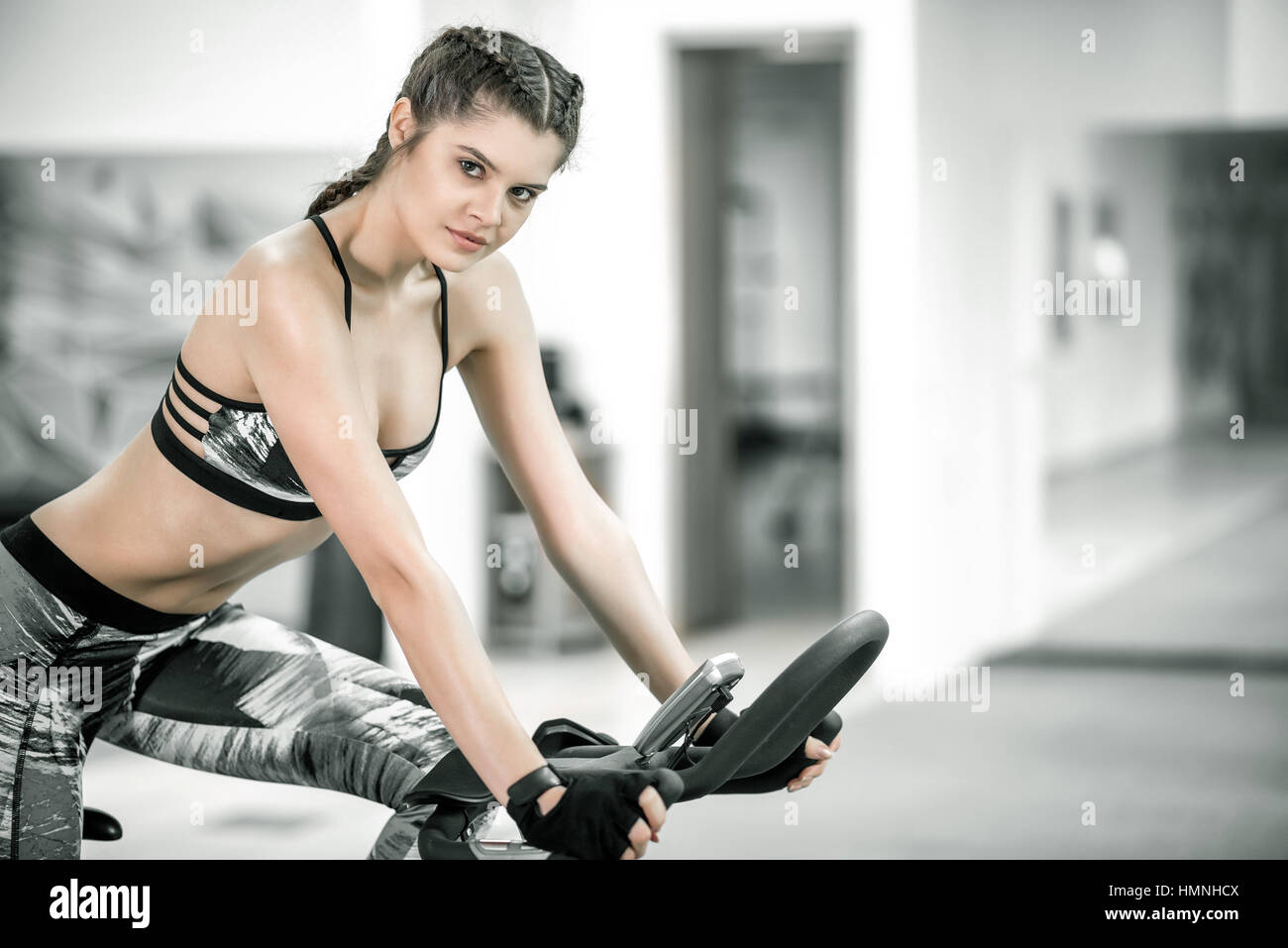 I giovani adulti caucasici femmina attraente con trecce utilizzando fitness bike nel moderno centro fitness. Tonica immagine. Foto Stock