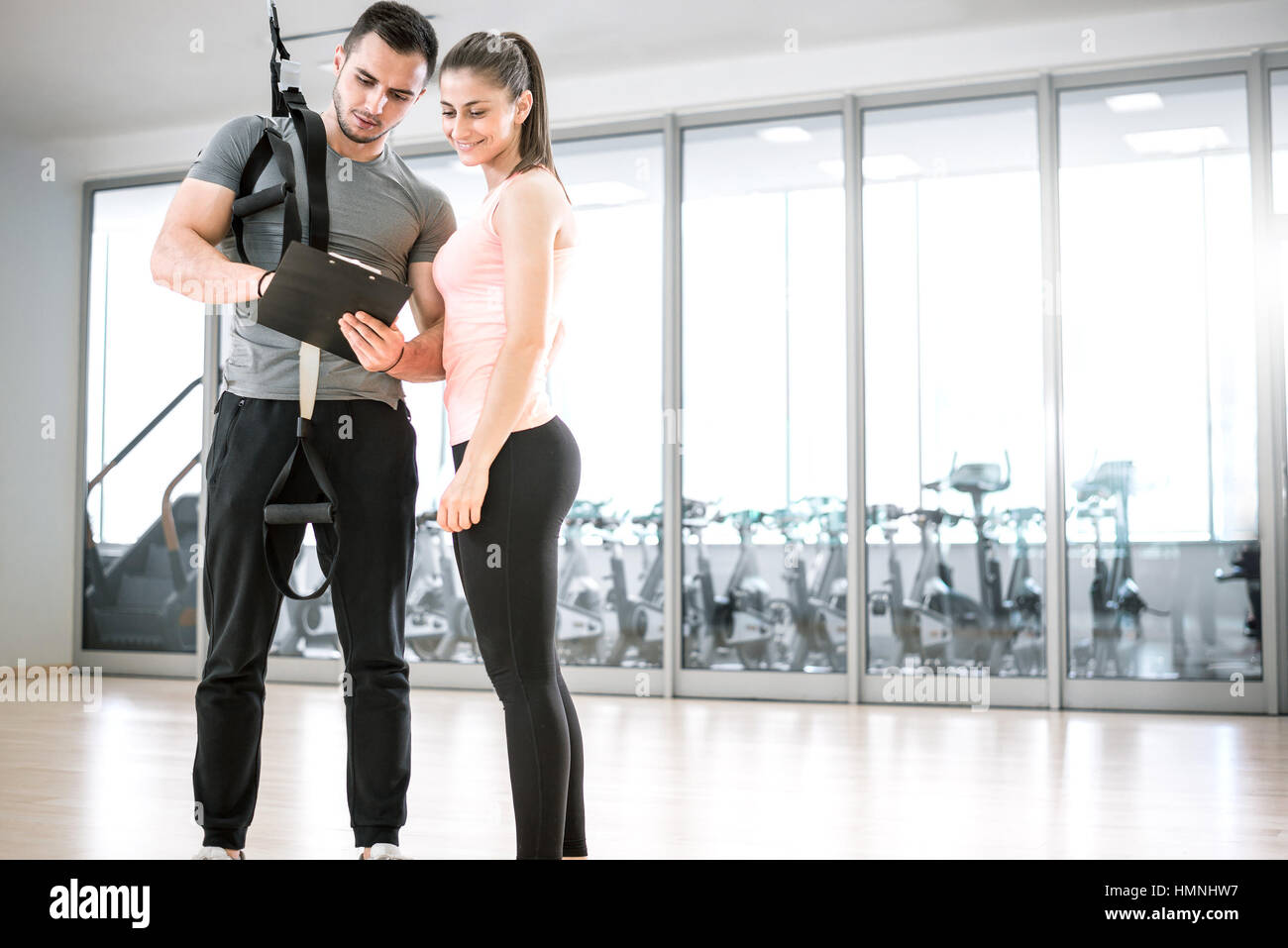 Personal trainer che mostra il risultato di un piano di formazione per i suoi giovani femmine client con corda di sospensione sulla spalla. Foto Stock