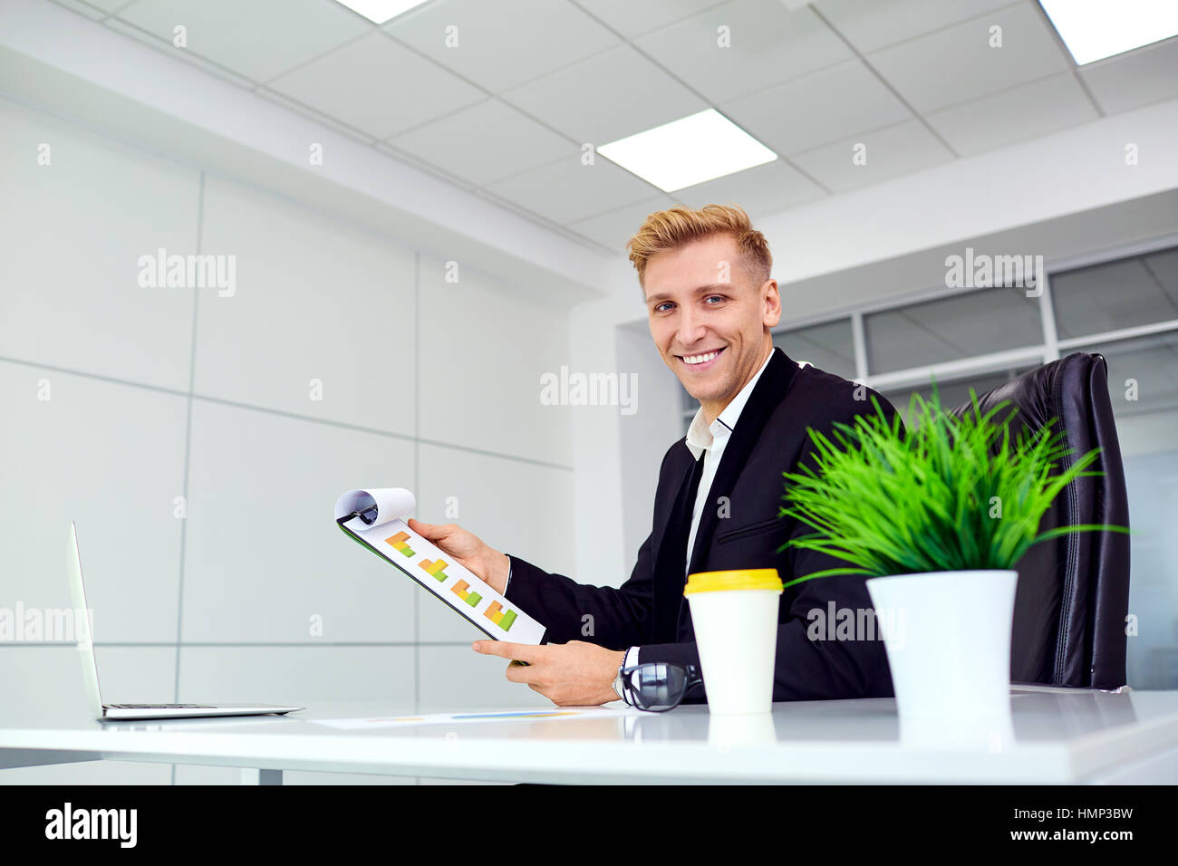 Imprenditore bionda sorridente per un computer portatile alla sua scrivania in ufficio Foto Stock