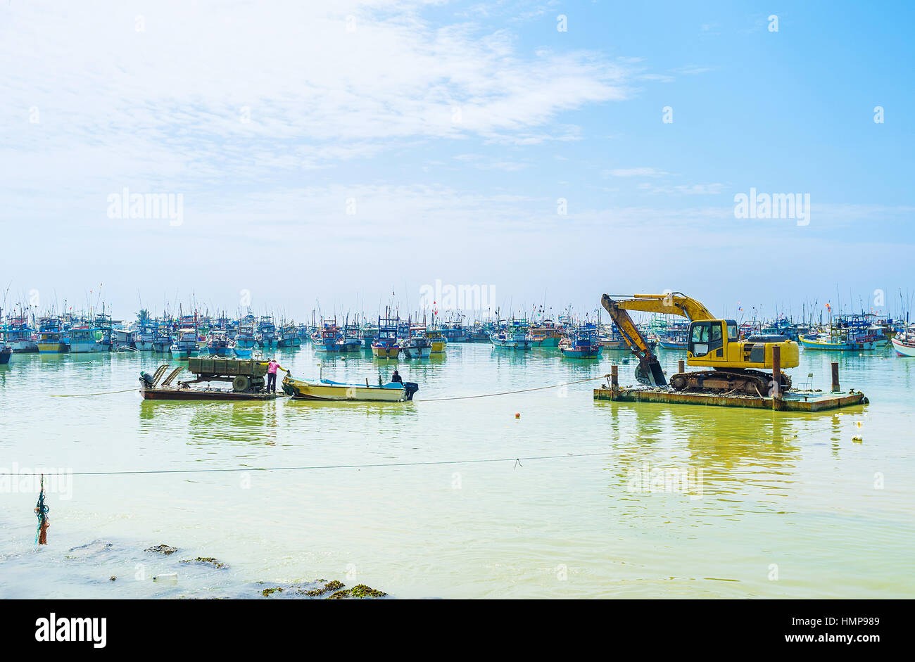 L'escavatore anfibio attende il vuoto del carico del rimorchio e la barca spinge il rimorchio, riempito con terra, alla riva, Mirissa, Sri Lanka. Foto Stock