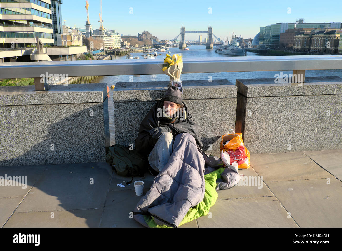 Vecchio uomo senza casa in inverno e caffè in tazza seduto Sacco a pelo sulla strada London Bridge con Tower Bridge e il Tamigi Londra UK KATHY DEWITT Foto Stock