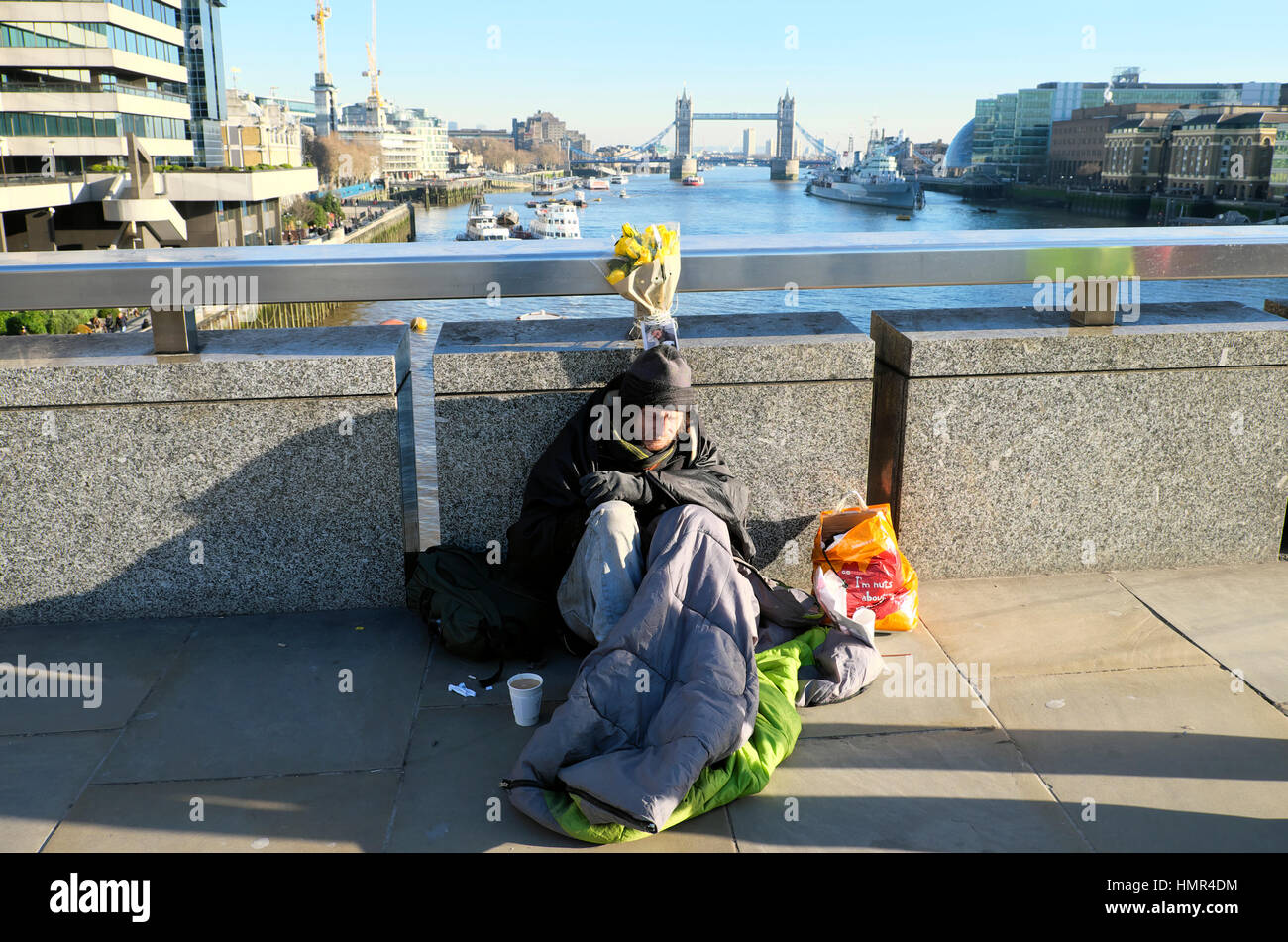 Senzatetto in una fredda giornata invernale seduta in sacco a pelo sul Ponte di Londra con una vista del Tower Bridge e il fiume Tamigi, Londra UK KATHY DEWITT Foto Stock