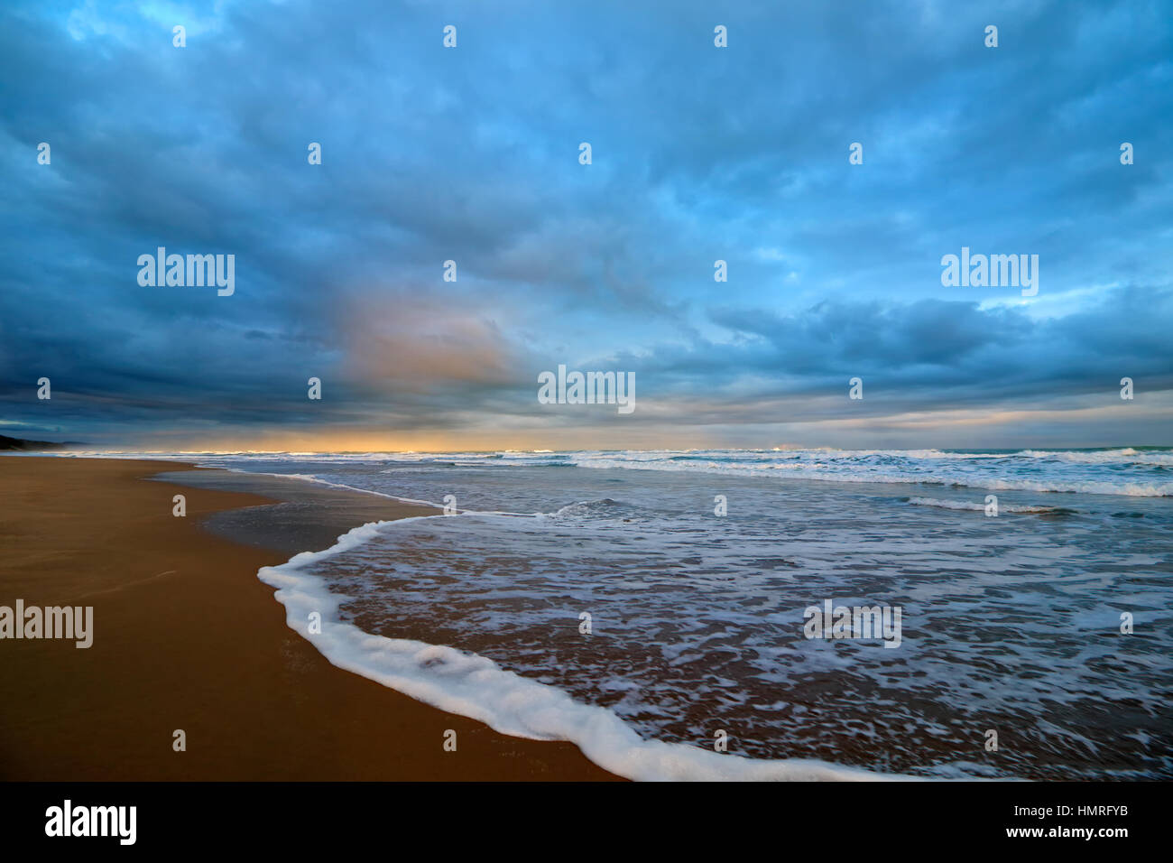 Seascape al tramonto con onde sulla spiaggia e pesante copertura nuvolosa Foto Stock