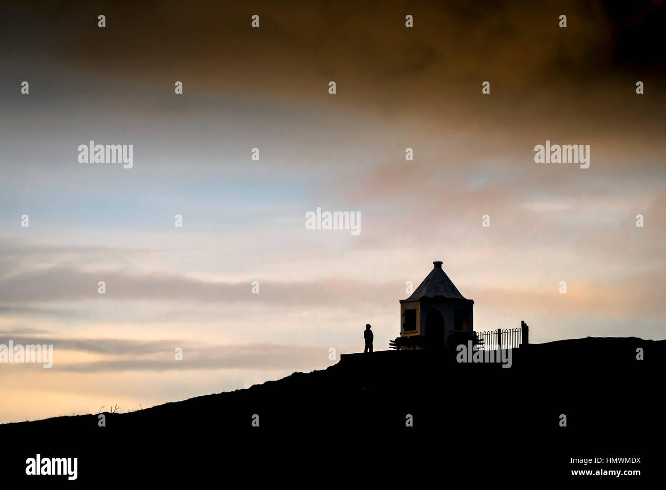 La silhouette di una persona in piedi al di fuori di un piccolo edificio in cima Towan promontorio in Newquay, Cornwall. Foto Stock