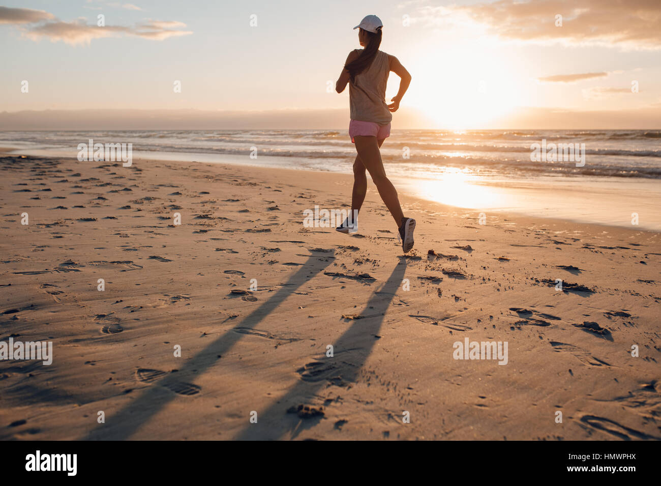 Vista posteriore del colpo di montare la giovane donna jogging sulla riva del mare nella mattina. Sani di sesso femminile che corre lungo la spiaggia. Foto Stock