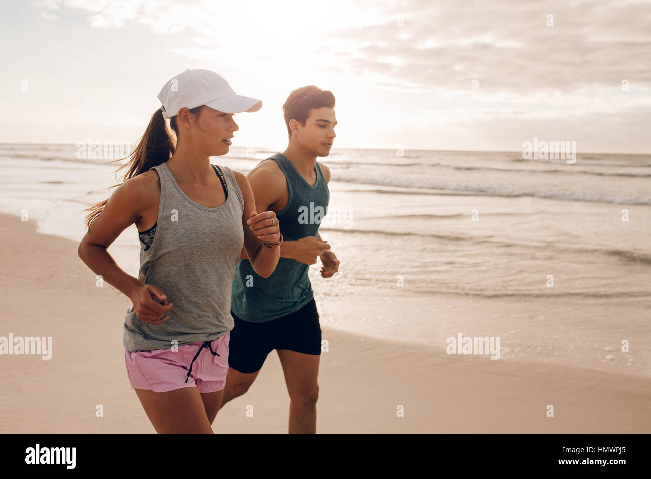Coppia giovane correndo insieme sulla spiaggia. Colpo all'aperto di una giovane coppia in corsa mattutina. Foto Stock