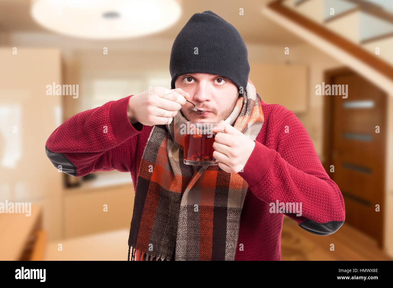 Giovane uomo in vestiti caldi gustando una tazza di acqua calda dolce tè in cucina Foto Stock