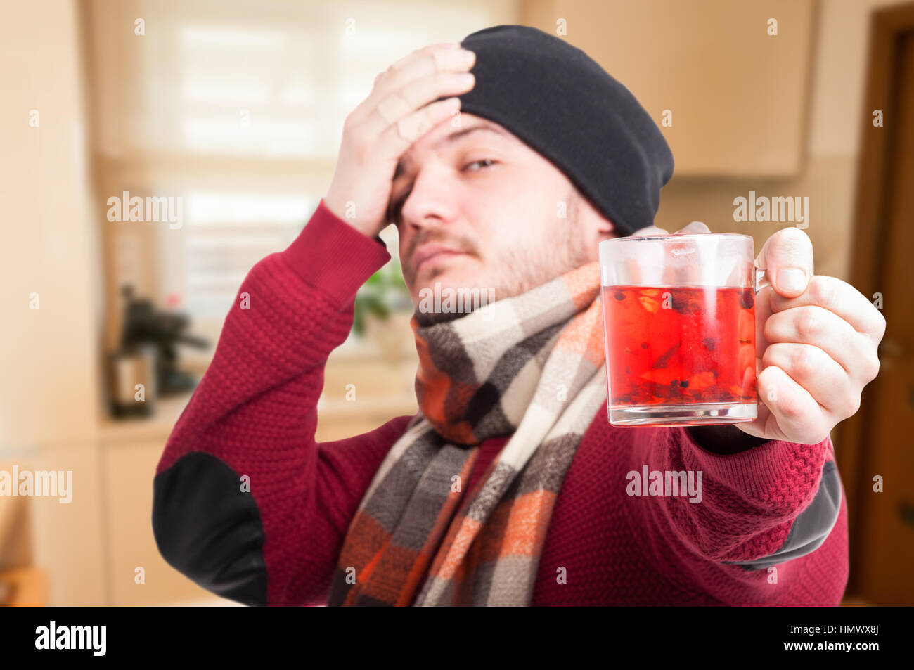 Uomo malato con sciarpa di bere il tè caldo che soffrono di mal di testa e influenza Foto Stock