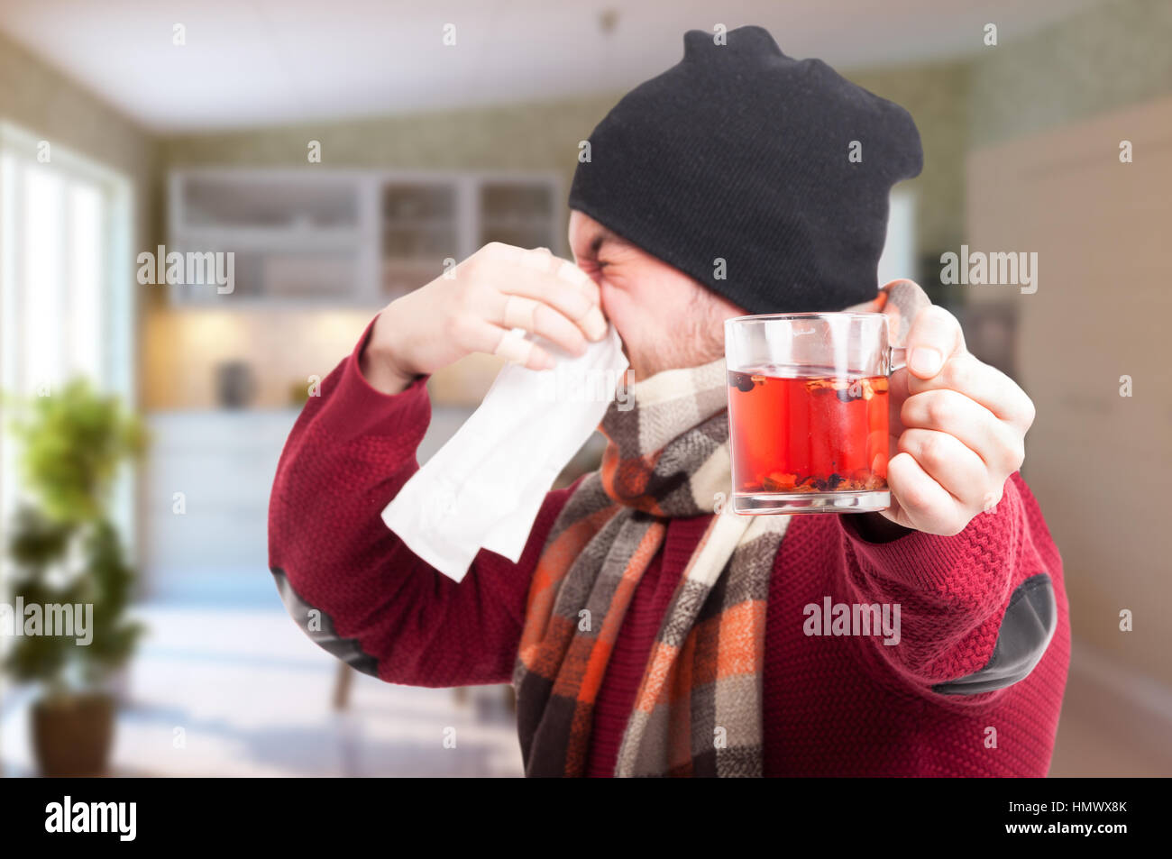 Giovane uomo con la tazza di tè soffia il naso come raffreddore e influenza concetto in casa Foto Stock
