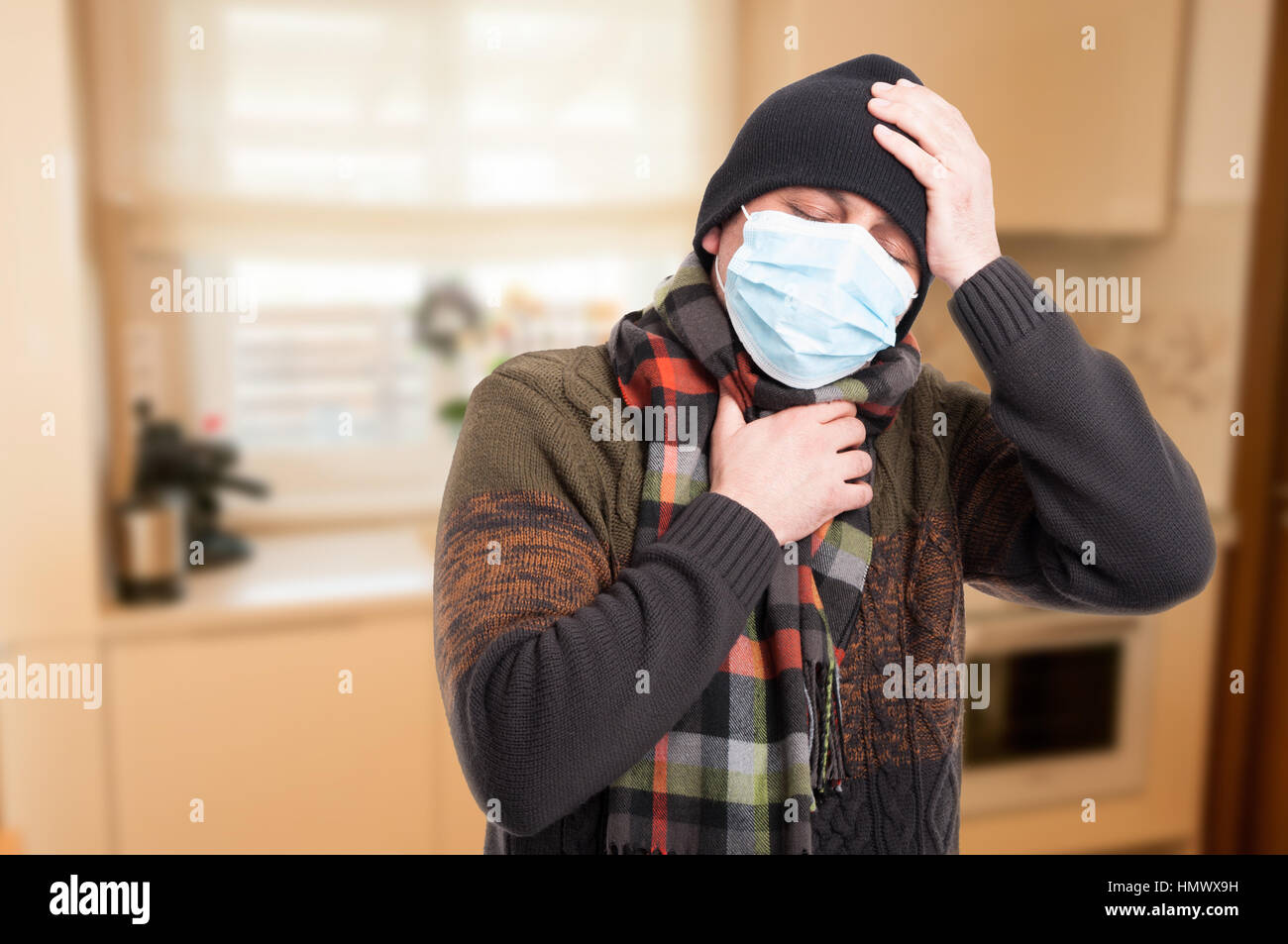 Uomo con influenza e mal di gola indossando maschera sterile all'interno della casa Foto Stock