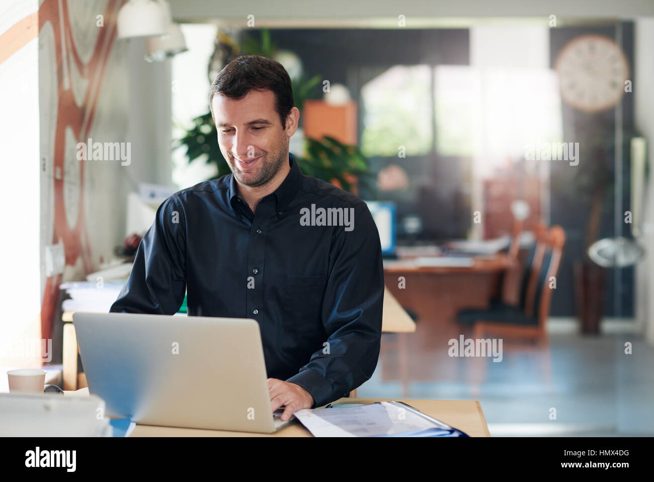 Sorridente imprenditore lavora su un laptop a una scrivania in ufficio Foto Stock