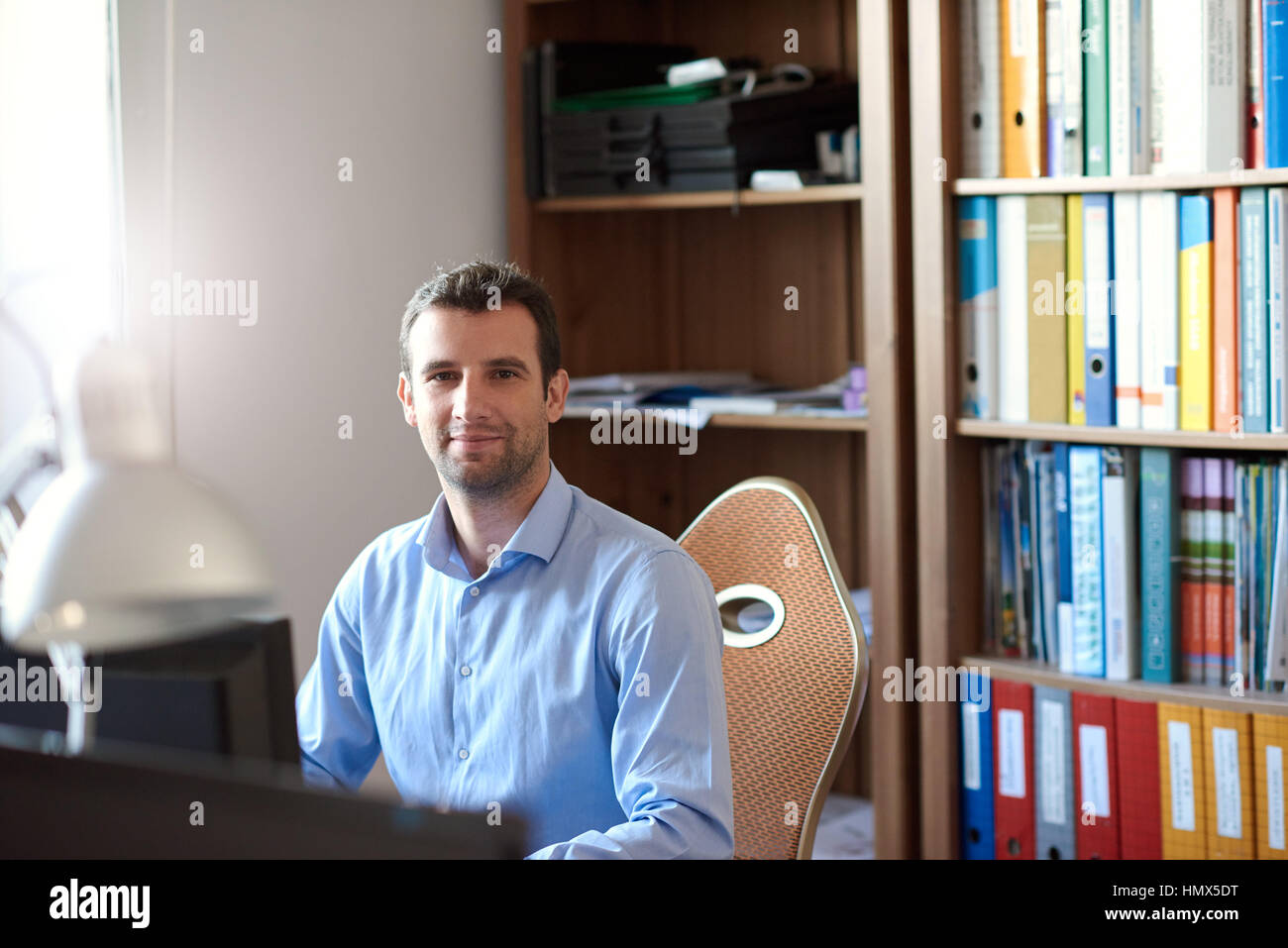 Ritratto di un fiducioso e imprenditore di successo che indossa un collare aperto shirt seduto alla sua scrivania e computer nel suo ufficio moderno Foto Stock