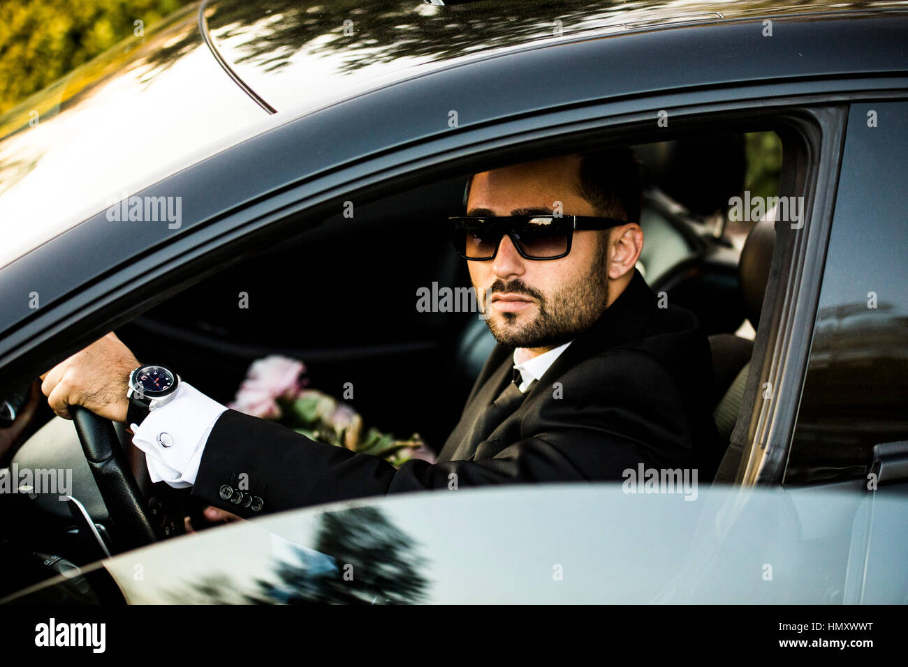 Bel ragazzo in abito nero in attesa la sua ragazza sulla strada. Con fiori. Foto Stock