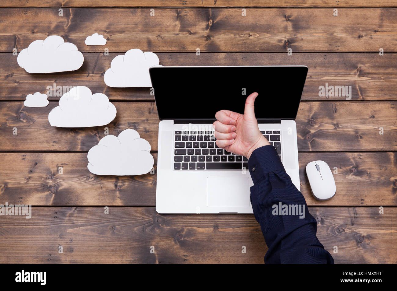 La tecnologia di cloud computing concetto con soffici nuvole accanto al computer portatile. Uomo con il pollice in alto sulla tastiera durante il caricamento dei dati su una tavola di legno Foto Stock