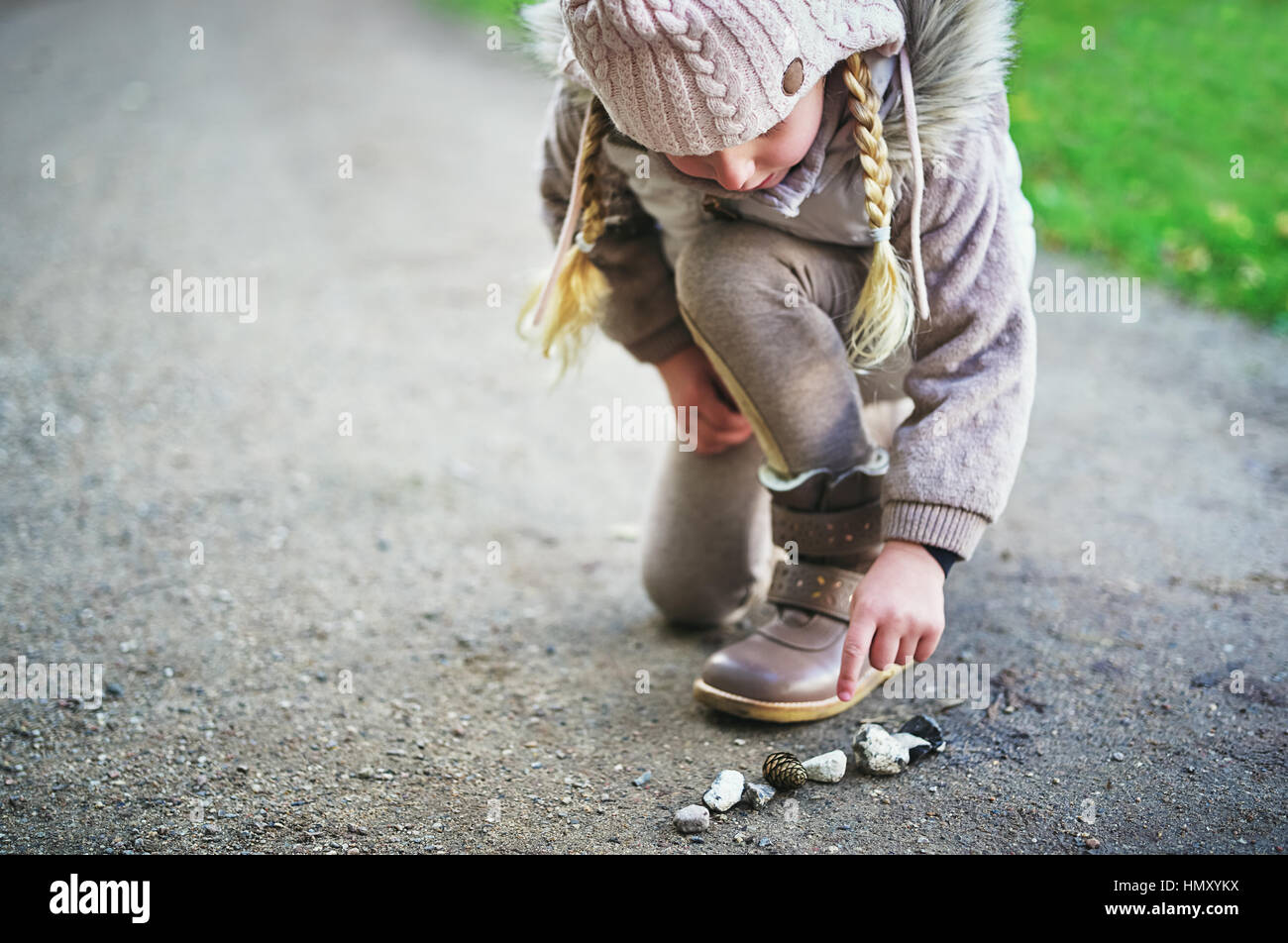 Piccolo bambino punti sui sassi sulla strada. All'aperto orizzontale shot Foto Stock