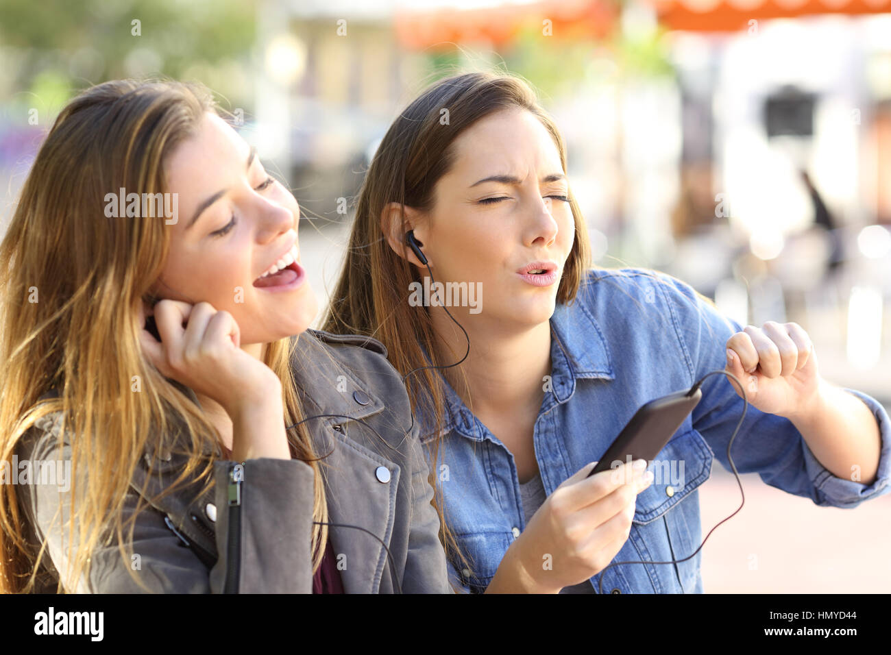 Amici di gioioso ascolto di musica on line da uno smart phone e cantando la condivisione di auricolari in strada Foto Stock