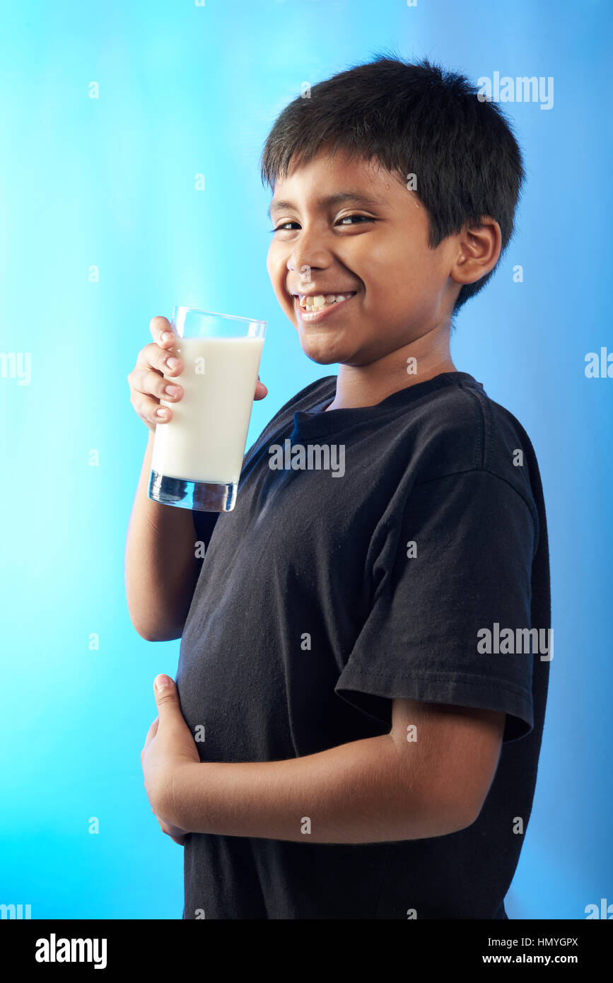 Sorridente chubby boy con un bicchiere di latte isolate su blu Foto Stock