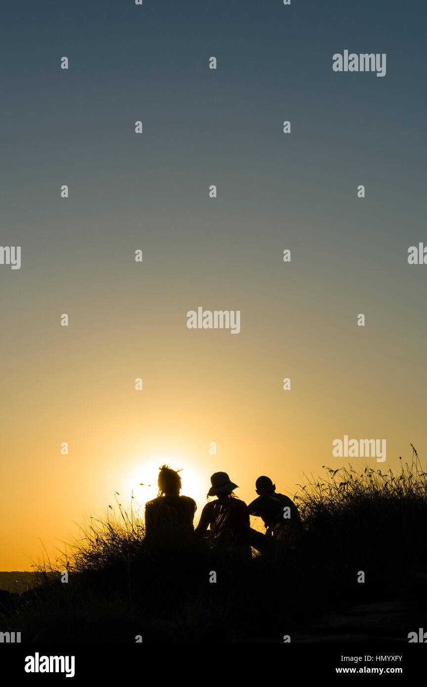 La silhouette di amici a guardare un famoso estremità superiore, il tramonto da una scarpata su una cassa di espansione. Foto Stock