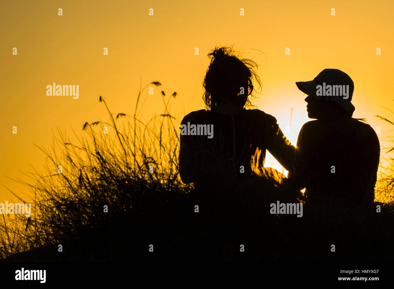 La silhouette di amici a guardare un famoso estremità superiore, il tramonto da una scarpata su una cassa di espansione. Foto Stock
