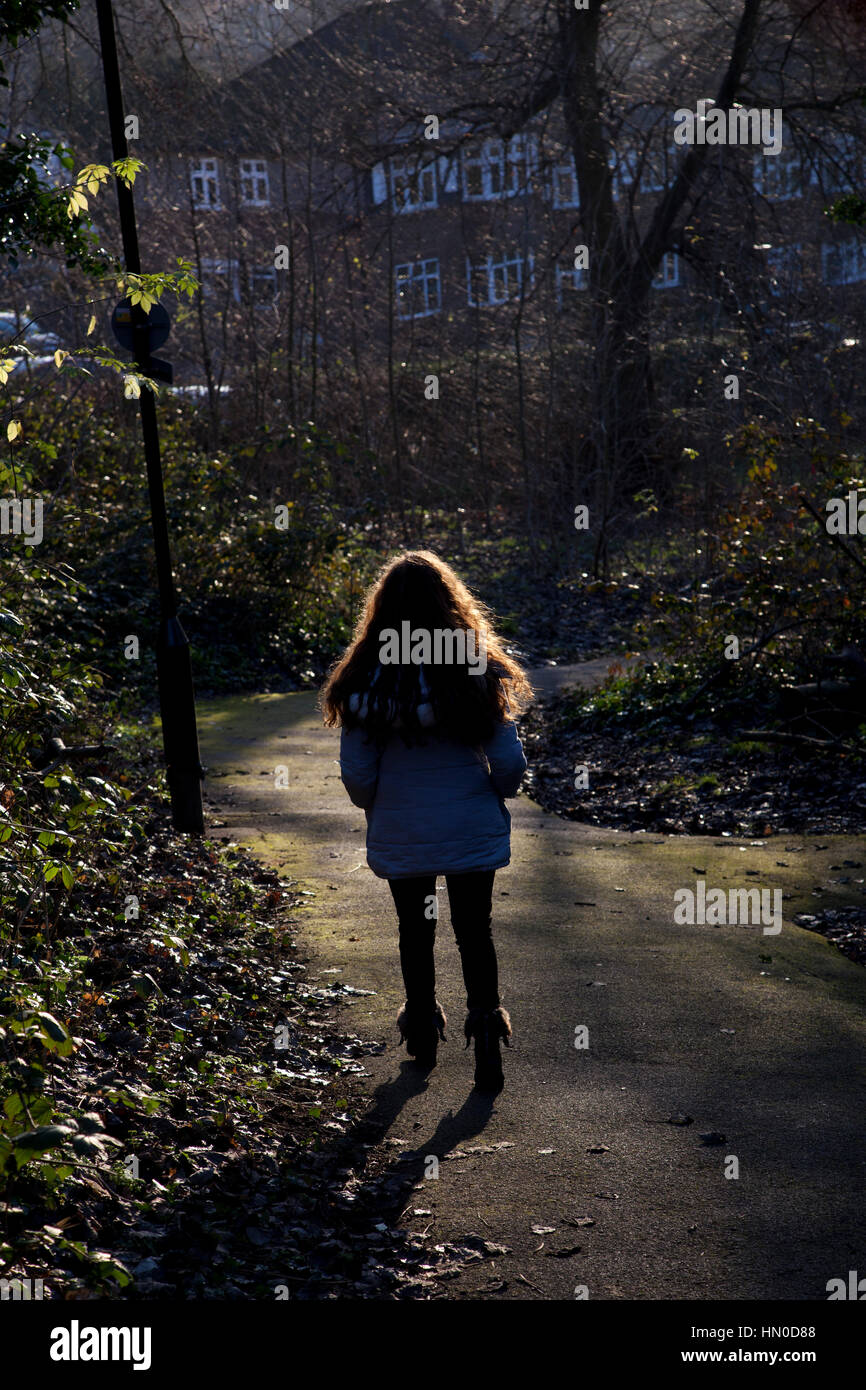 A seguito di una giovane donna a piedi attraverso un parco. Vista posteriore. Foto Stock