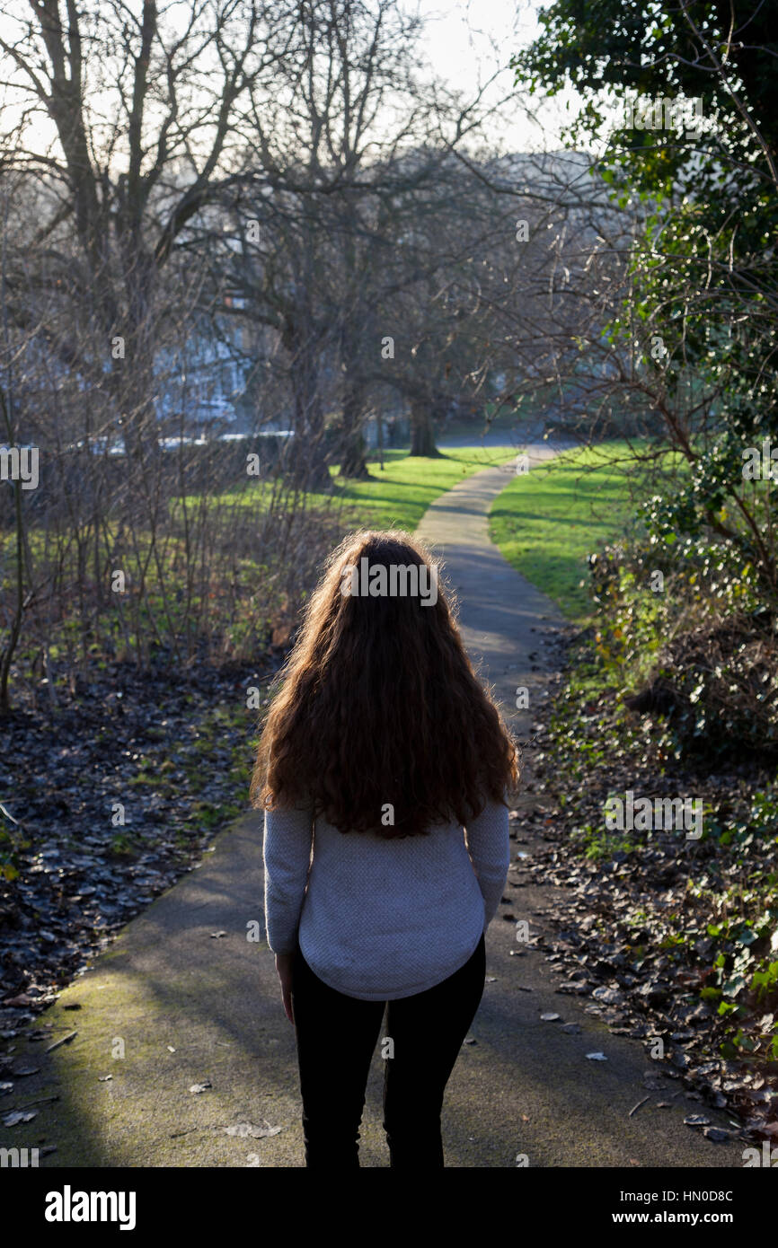 Vista posteriore del colpo di una giovane donna che cammina lungo un parco attraverso un parco. Foto Stock