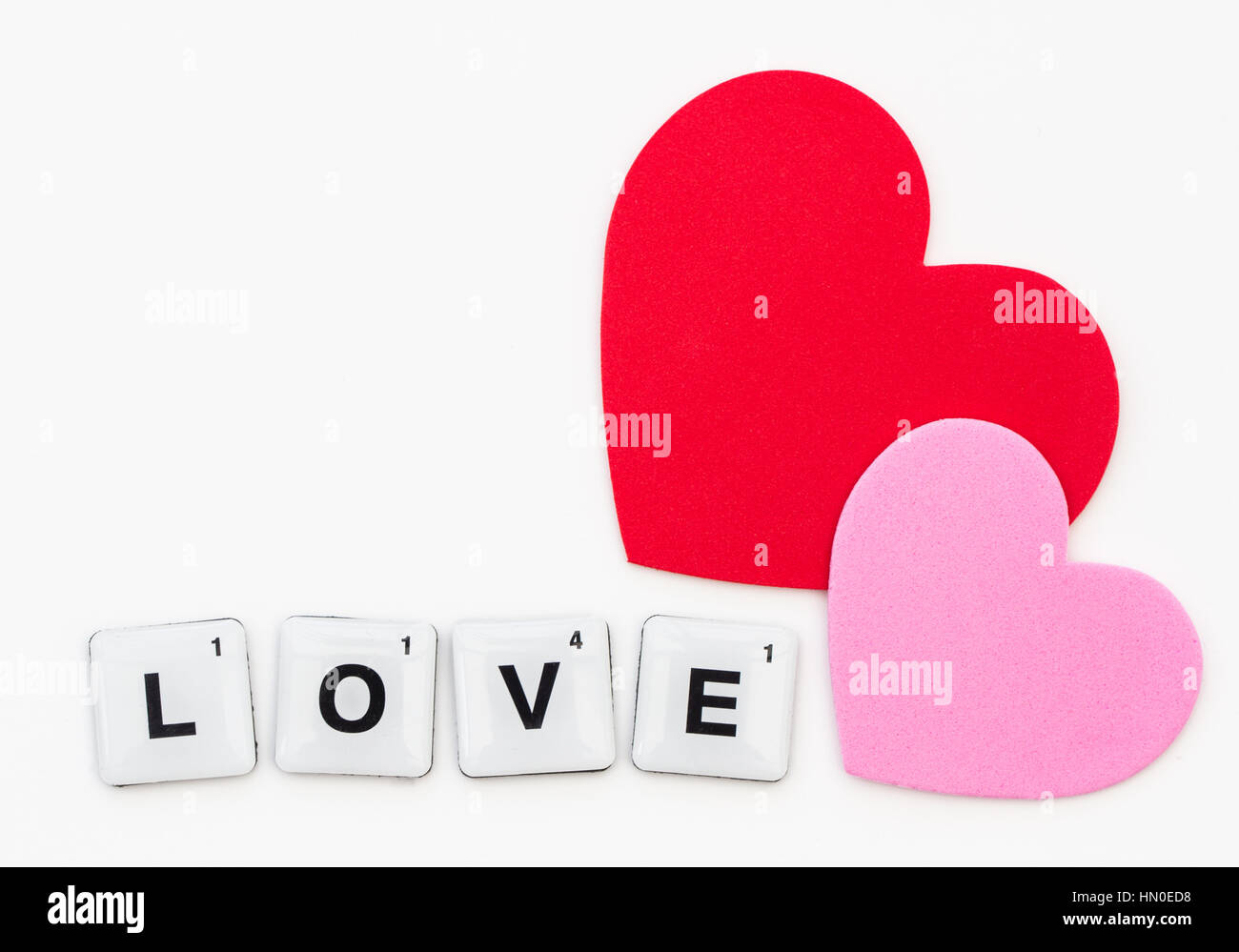 La parola amore ha creato dalla lettera piazze o piastrelle scrabble isolato su un fondo bianco con cuori e copia di spazio. Foto Stock
